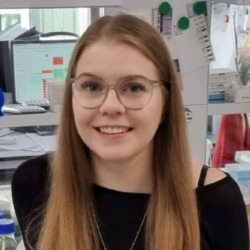 Porträtaufnahme einer Mitarbeiterin vor einem Arbeitsplatz im Labor.