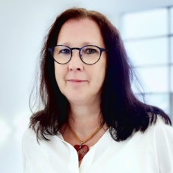 Portr&auml;t einer Mitarbeiterin mit dunklen Haaren und Brille vor hellem Hintergrund.