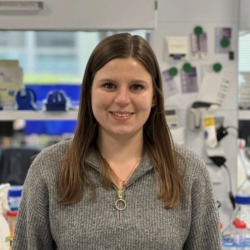 Porträt einer Mitarbeiterin in einem Laborumfeld mit Geräten im Hintergrund.